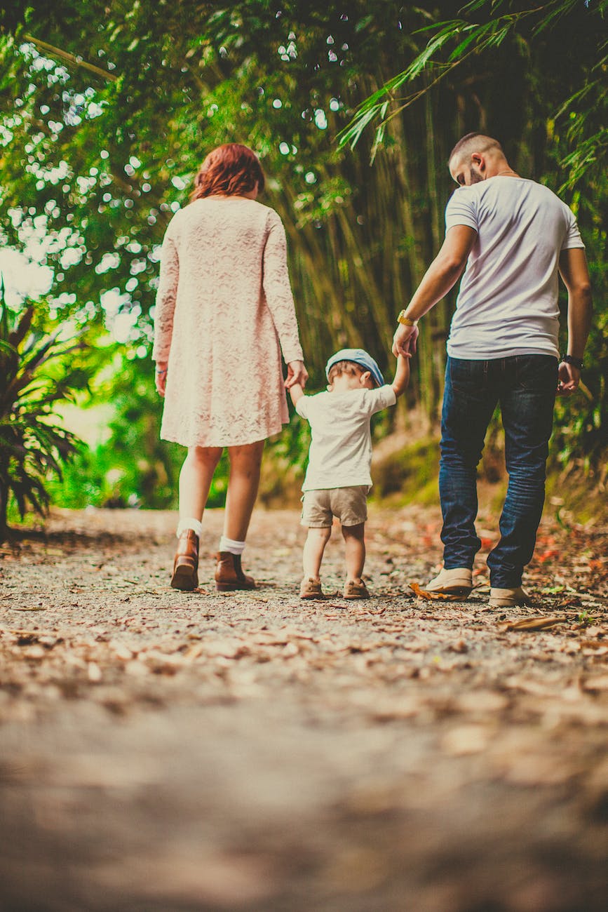 low angle shot of a child held by woman and man on on each hand walking on an unpaved pathway outdoors